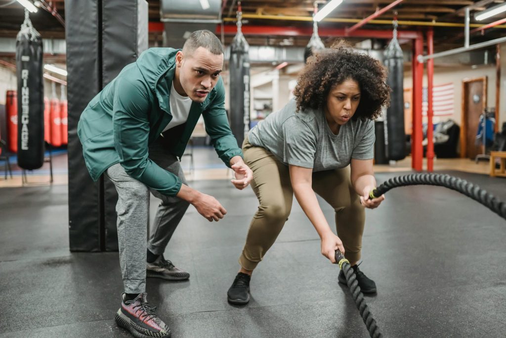 A dedicated woman focuses on battle rope training, guided by her fitness coach.
